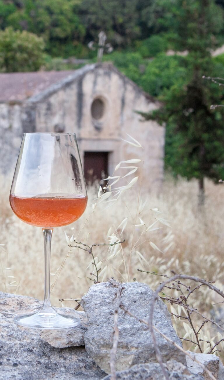 A glass of orange wine perched on a rock with an old church in the background, capturing the essence of tradition and beauty in orange wine culture.