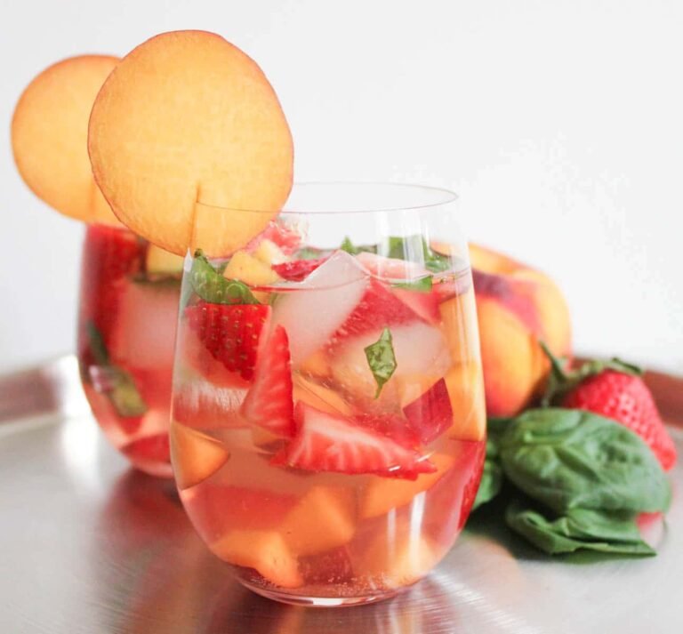 Refreshing rosé sangria with peach slices, strawberries, and basil leaves in two glasses on a silver tray
