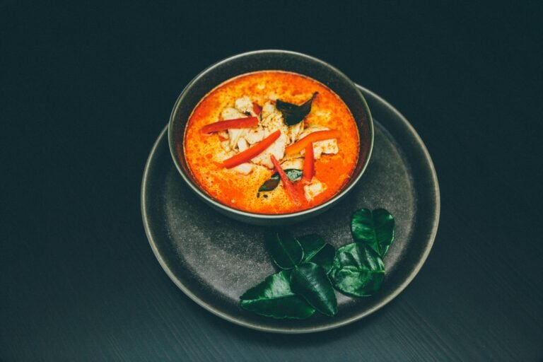 A bowl of traditional Hungarian fish soup, rich in flavour and vibrant in colour, garnished with fresh herbs, served hot.
