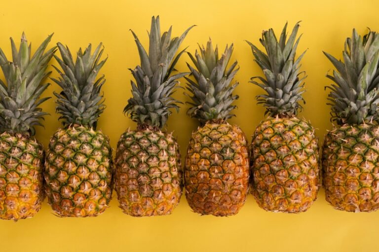 Row of fresh pineapples against a bright yellow background