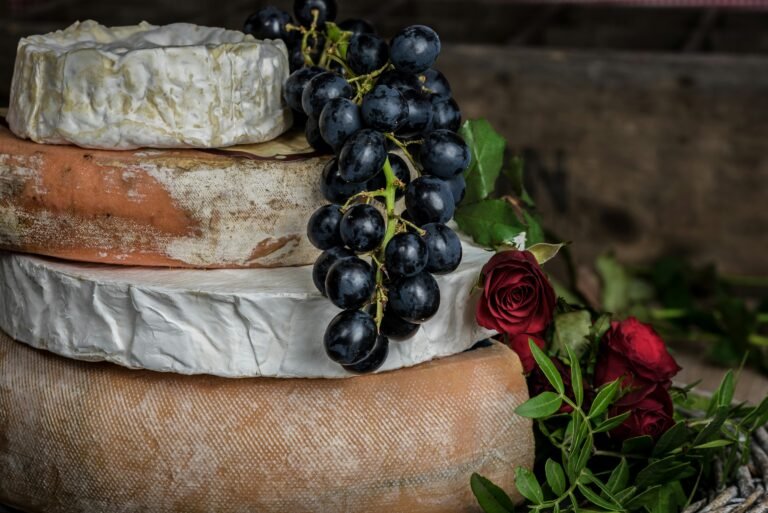 Close-up of aged cheeses stacked with a bunch of dark grapes and red roses