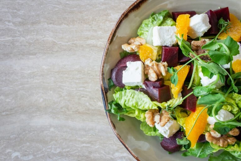Fresh salad with lettuce, beets, oranges, walnuts, and feta cheese on a ceramic plate