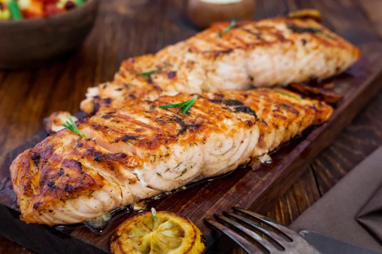 Delicious grilled salmon fillets seasoned with herbs and served with lemon slices on a wooden board
