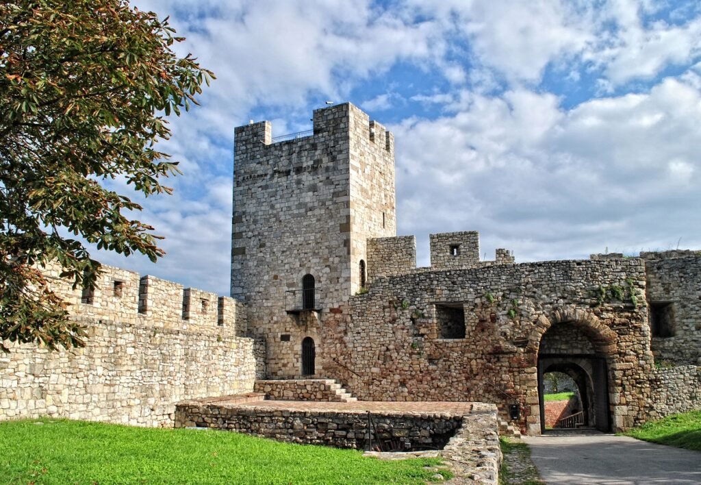 View of Kalemegdan Fortress with its stone walls and tower, surrounded by greenery and under a partly cloudy sky