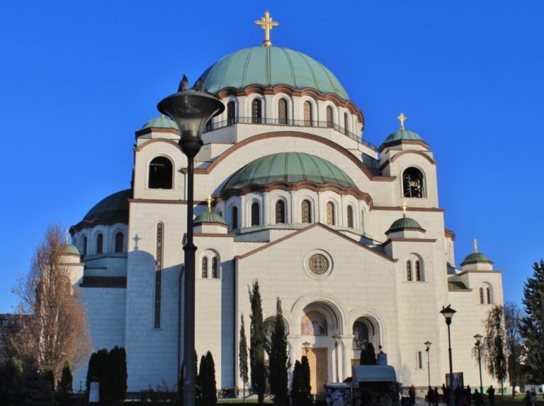 Front view of the Church of Saint Sava in Belgrade with its green domes and white facade under a clear blue sky