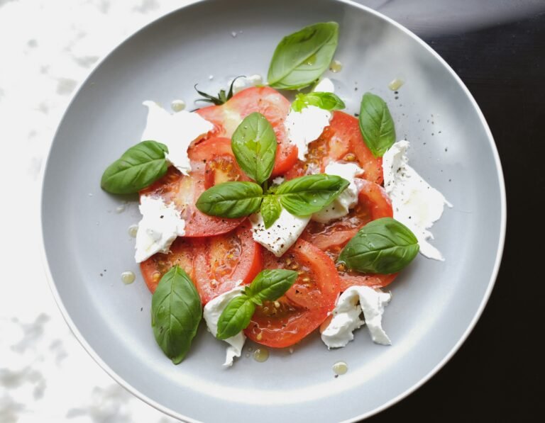 Caprese salad with fresh tomatoes, mozzarella, and basil on a white plate, a popular Italian summer appetizer