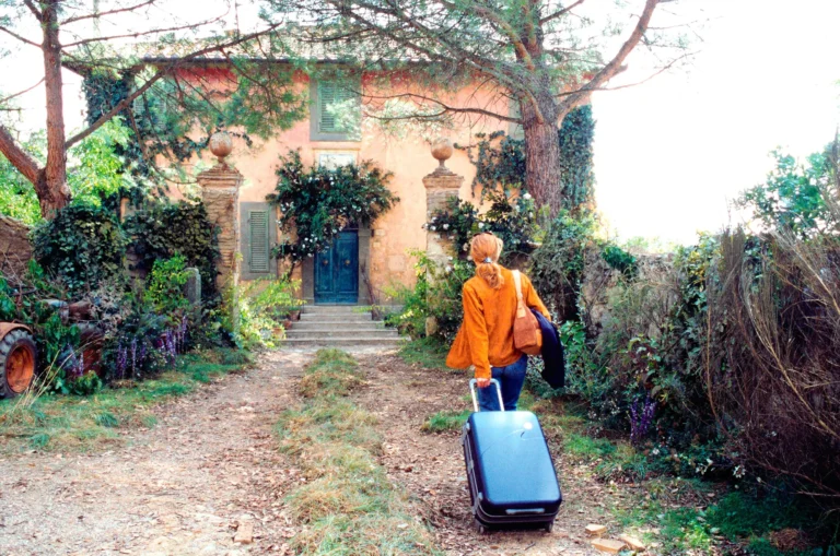 The protagonist of the movie Under the Tuscan Sun holding a suitcase while entering a cabin located in the Tuscany area.