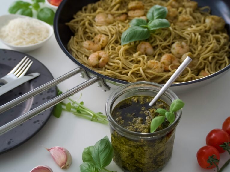 Pesto pasta with shrimp served in a pan with a jar of fresh pesto sauce and basil garnish