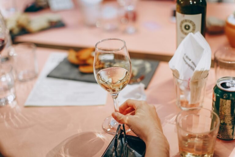 A woman holding a glass of white wine against a pink background.