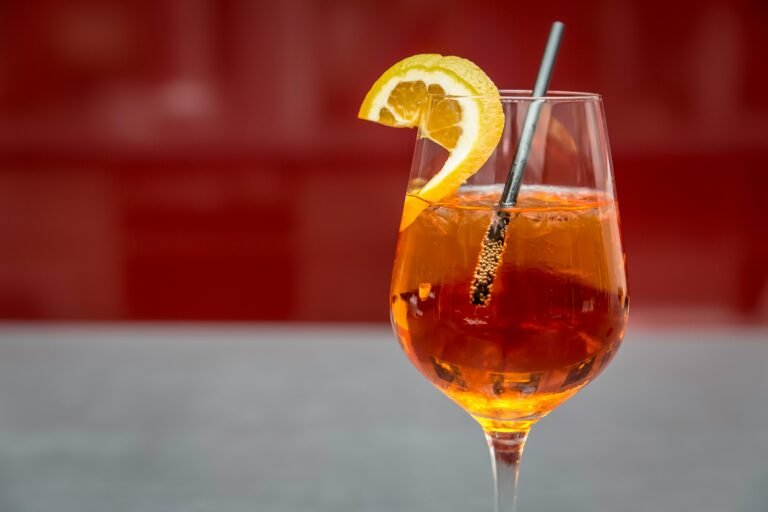 Refreshing Aperol Spritz cocktail with orange slice garnish on a red background