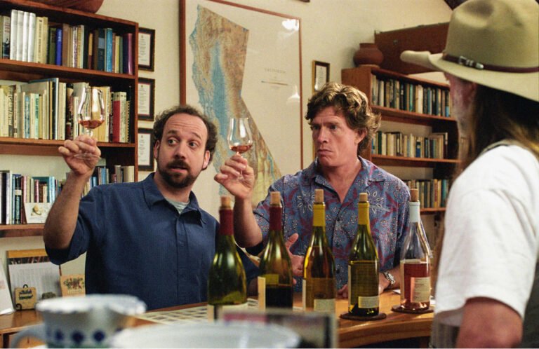 Scene from a movie showing two men tasting wine in a library.