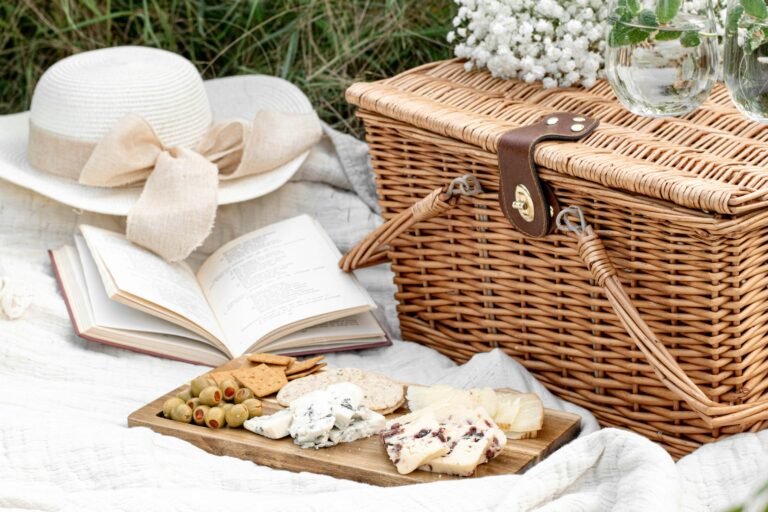 Picnic basket with cheese board on white blanket in summer