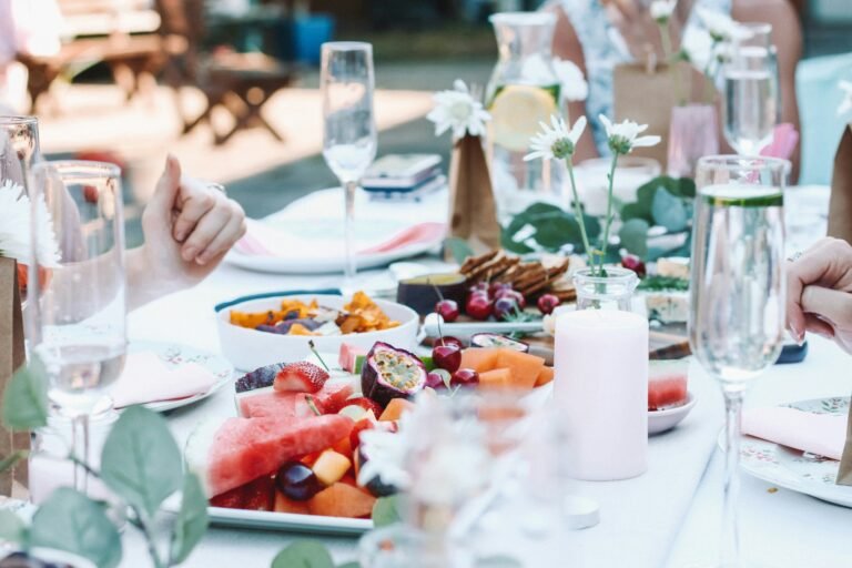 Group of friends enjoying a summer dinner by the lake with wine and food on a wooden deck.