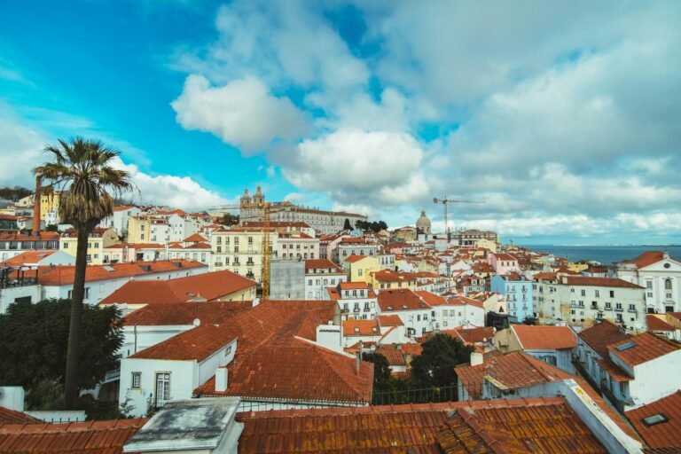 A panoramic view of the rooftops and historic buildings of Lisbon, Portugal, under a vibrant blue sky.