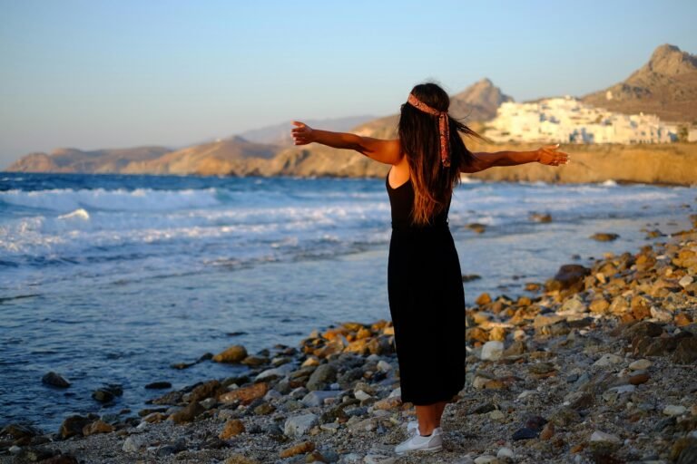 Woman enjoying the breeze with open arms on a rocky beach in Greece.