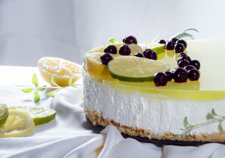 No-bake lemon cheesecake topped with fresh lime slices and berries, set on a white cloth background.