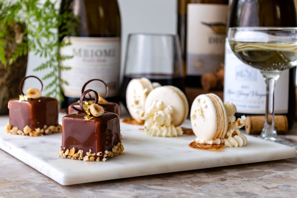 Chocolate-covered hazelnut desserts and macarons with wine pairing, served on a marble platter with wine bottles in the background.