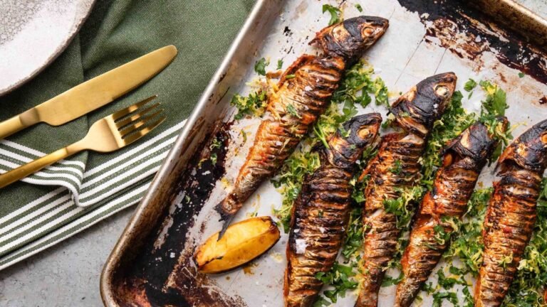 Grilled fish with charred skin served on a tray with lemon and fresh herbs.