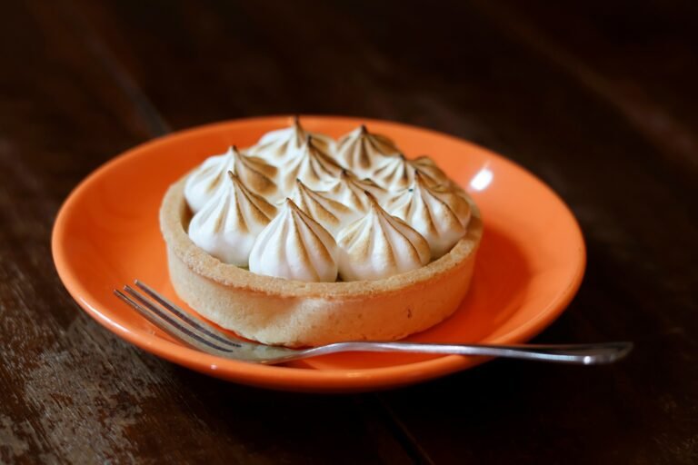 Lemon tart with toasted meringue peaks, served on an orange plate with a fork.