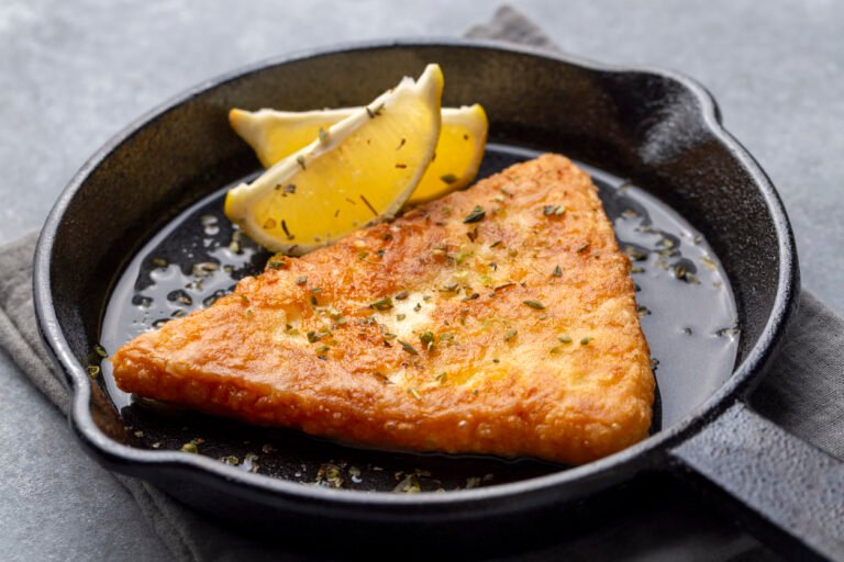 Crispy saganaki cheese garnished with lemon wedges in a cast-iron skillet.