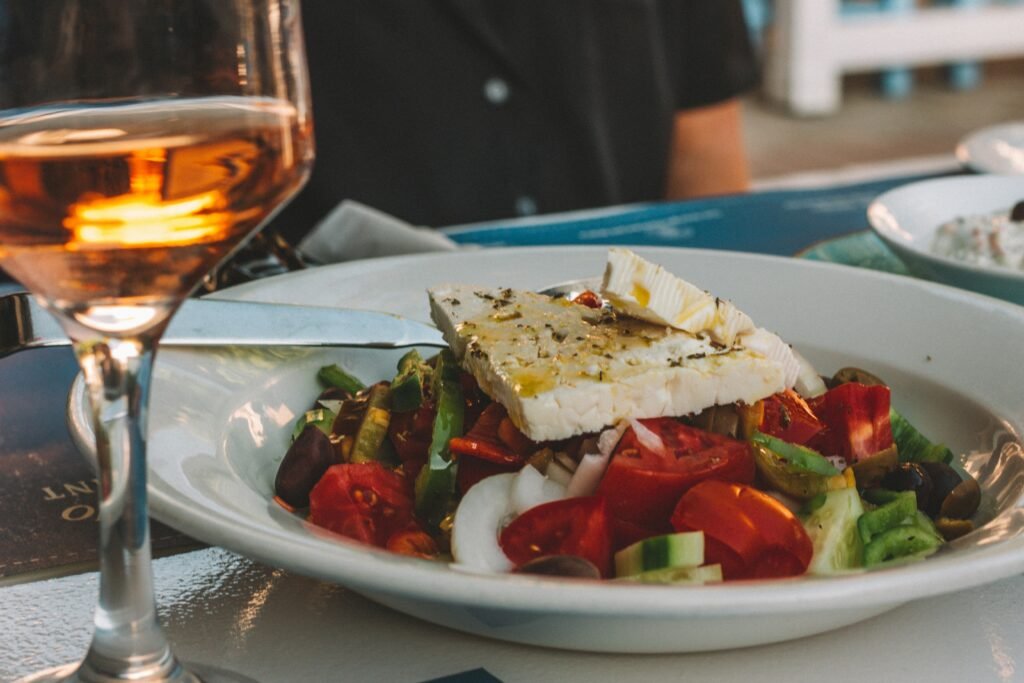 Fresh Greek salad with feta cheese, tomatoes, cucumbers, and olives, served with a glass of rosé wine.