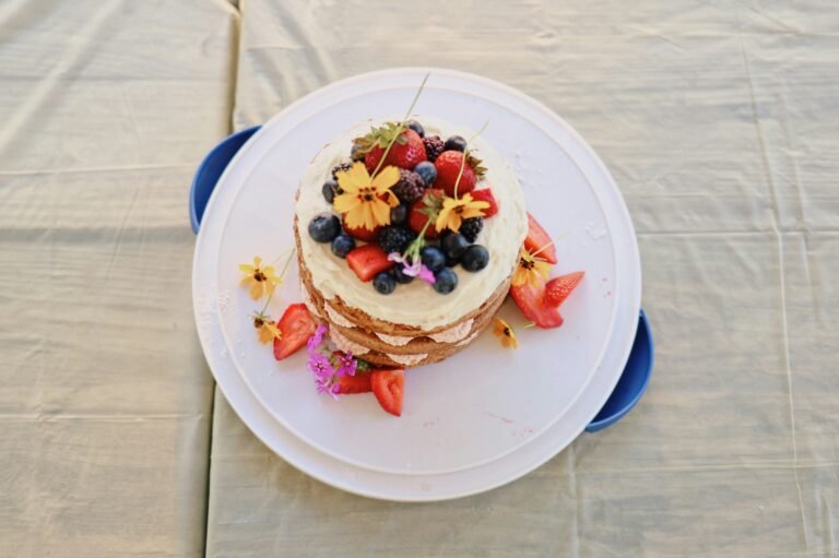 Summer fruit cake decorated with fresh berries and edible flowers, viewed from above.