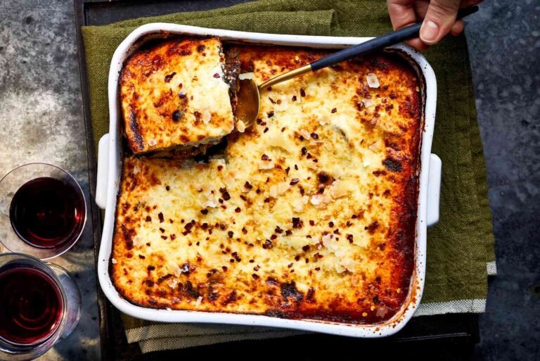 Traditional Greek moussaka in a baking dish with a golden-brown top layer, served with red wine.