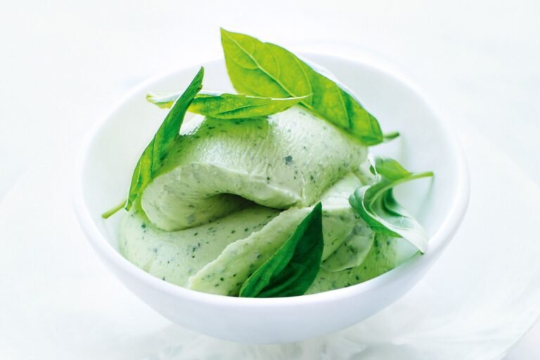 Smooth basil ice cream with fresh basil leaves, served in a white bowl on a light background.