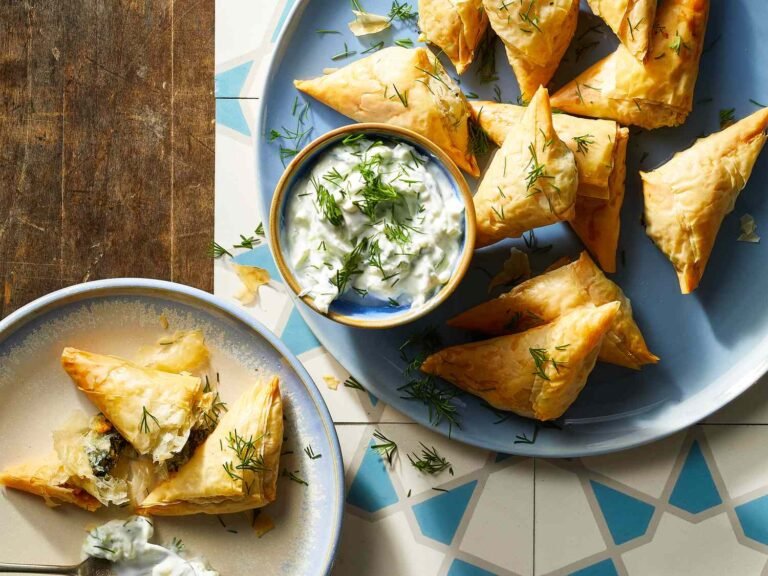 Spanakopita triangles served with a bowl of creamy dill sauce on a blue plate.