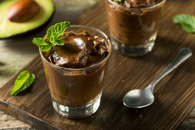 Rich and creamy chocolate avocado mousse served in a glass, garnished with fresh mint leaves, with an avocado in the background.