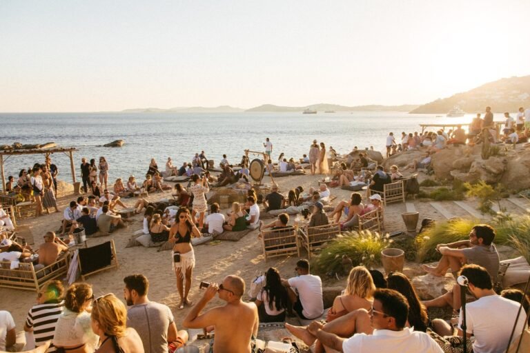 Crowd enjoying a lively beach party at sunset with the ocean in the background.