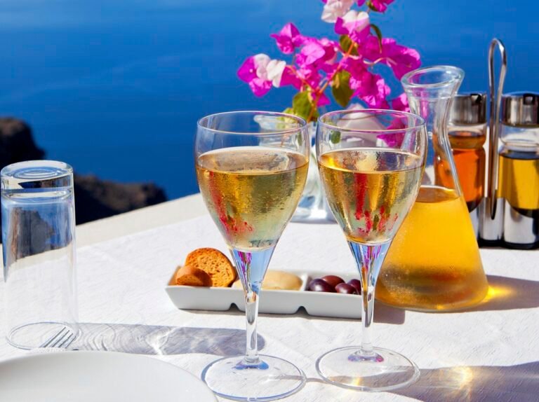 Breakfast setup with wine glasses and a carafe of juice against a backdrop of the sea.