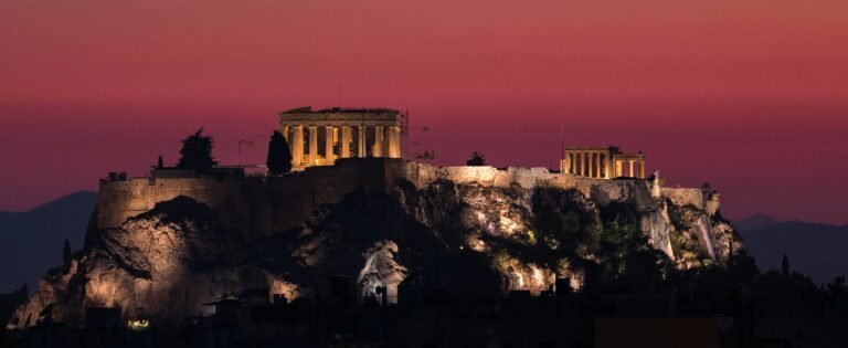 The illuminated Acropolis of Athens against a vibrant pink sunset sky.