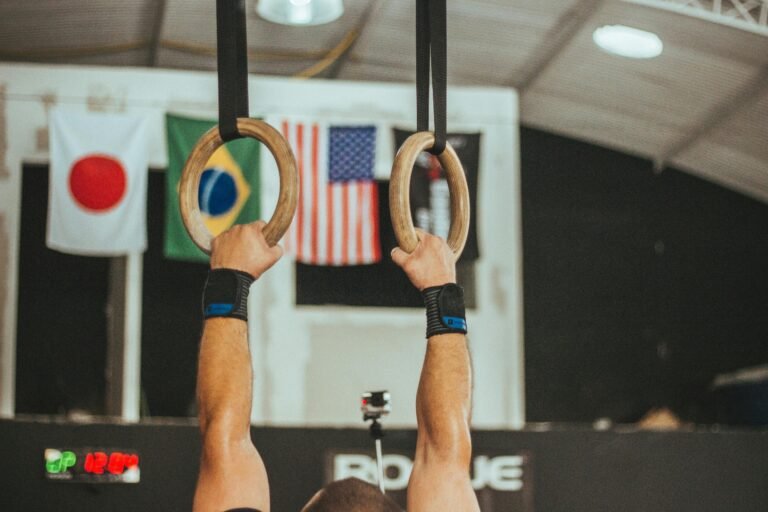 Athlete gripping gymnastics rings with international flags in the background.