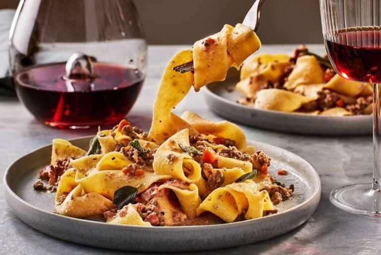 Delicious pappardelle pasta paired with a glass of red wine in an elegant dining setting.