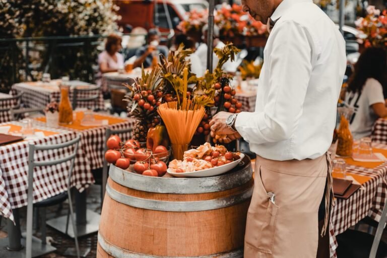 Outdoor Italian restaurant with a display of fresh pasta, tomatoes, and wine, attended by a server in Rome.