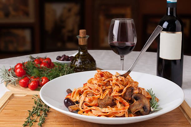 Hearty plate of tagliatelle pasta with a savory mushroom and tomato sauce, accompanied by a glass of red wine.