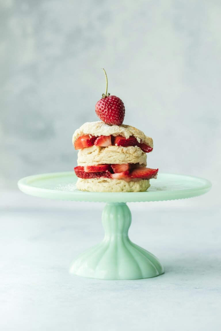 Freshly baked strawberry shortcake displayed on a blue cake stand, topped with whipped cream and vibrant red strawberries.