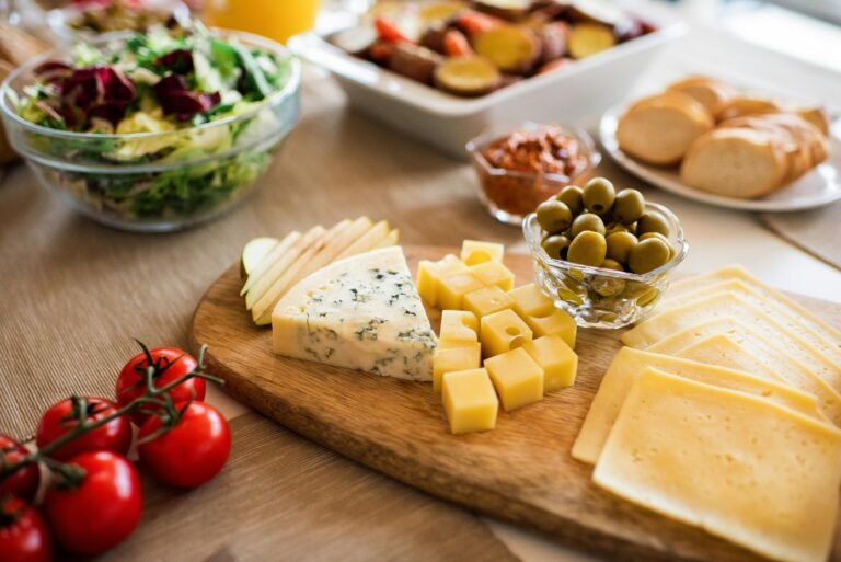 A cheese platter with a variety of cheeses, olives, and fresh salad served on a wooden board.