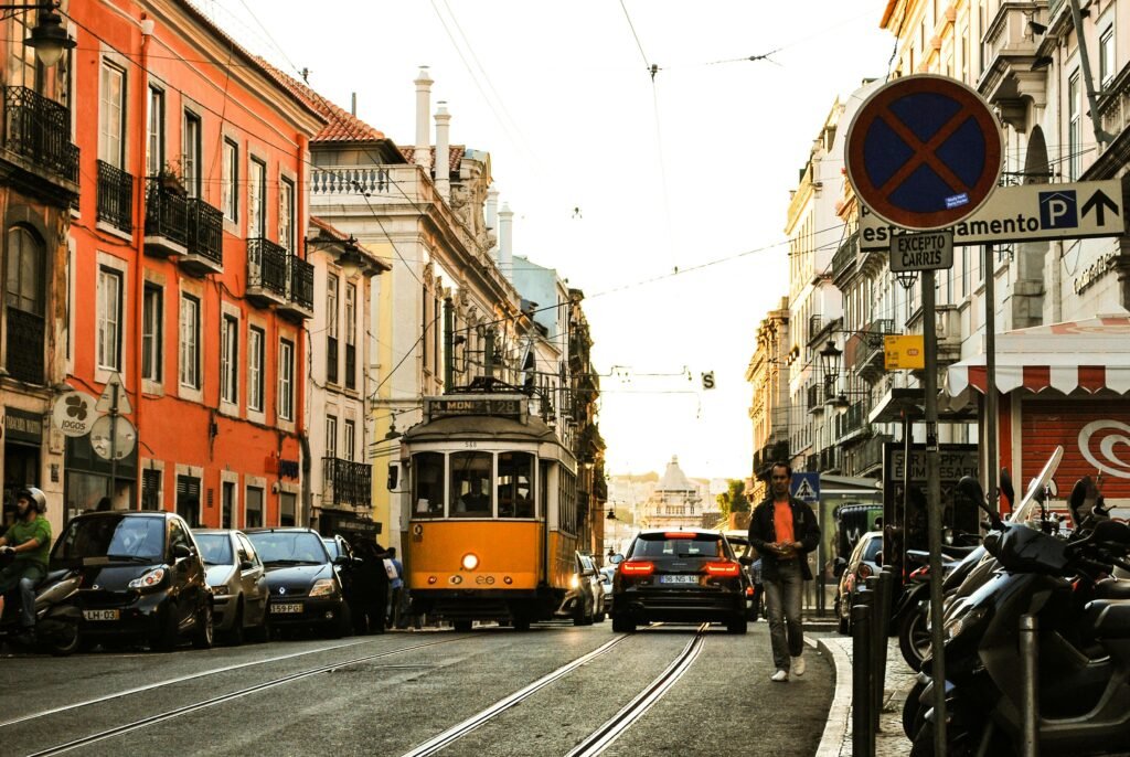 A traditional yellow tram navigating through the charming streets of Lisbon, Portugal at sunset.