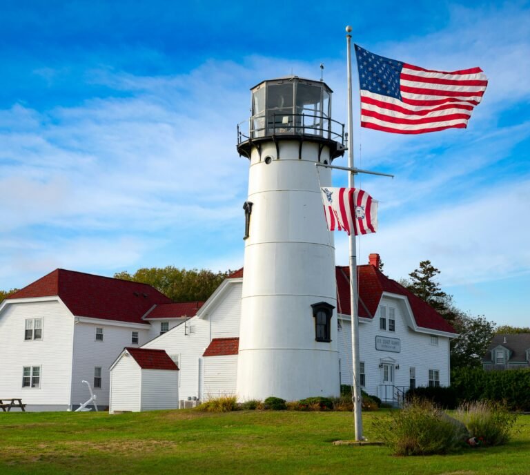 Classic white lighthouse standing tall on the U.S. coastline, with a bright blue sky and ocean waves crashing below.