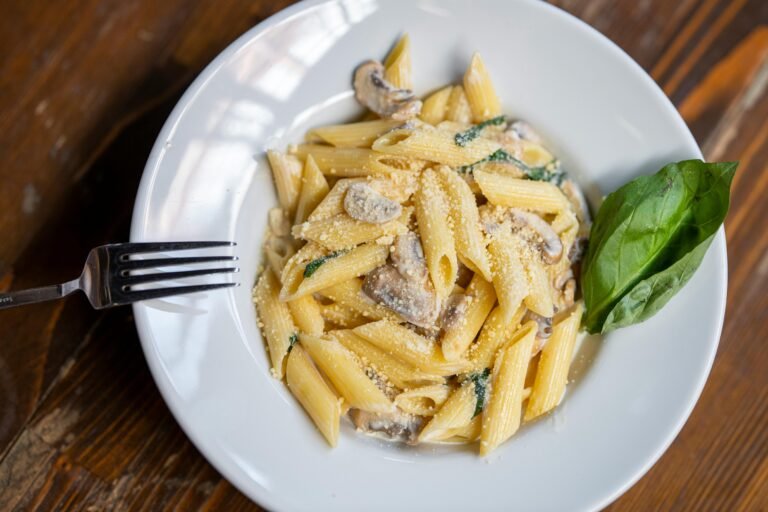 Creamy pasta with mushrooms and Parmesan cheese garnished with a basil leaf.