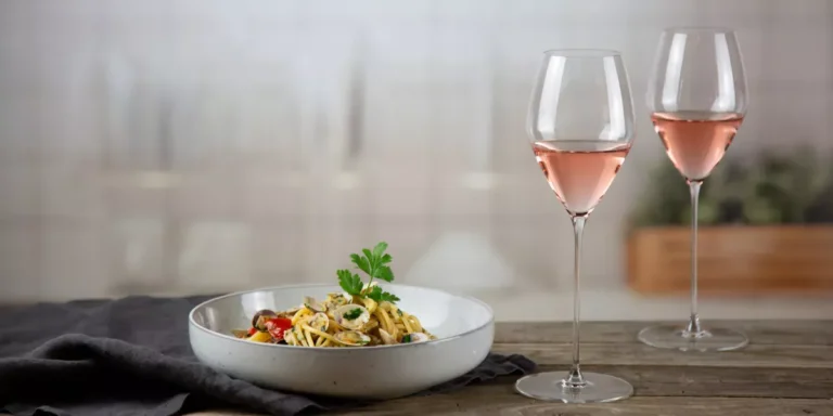 Two glasses of rosé wine paired with a plate of seafood pasta, served on a rustic wooden table.