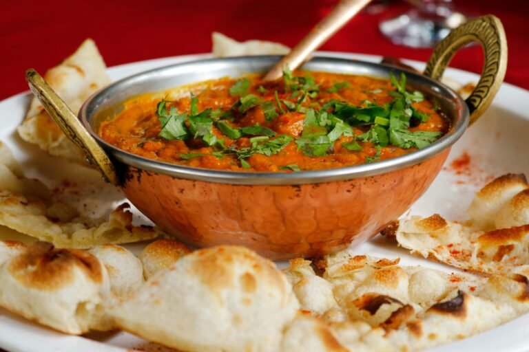 Indian curry in a copper bowl garnished with cilantro, served with naan bread.