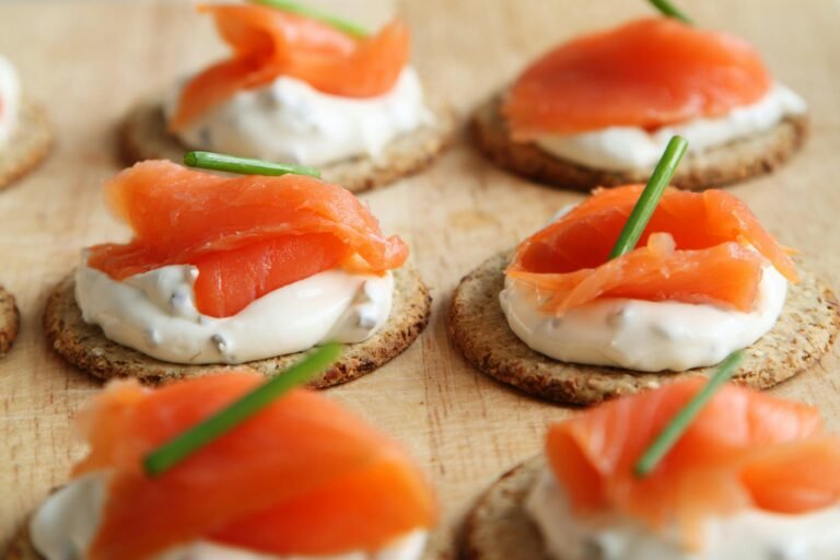 Smoked salmon on crackers with cream cheese and a chive garnish.