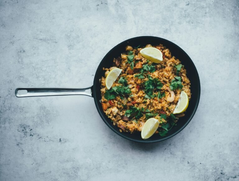 A top view of a pan filled with Spanish-style paella garnished with lemon wedges and fresh parsley