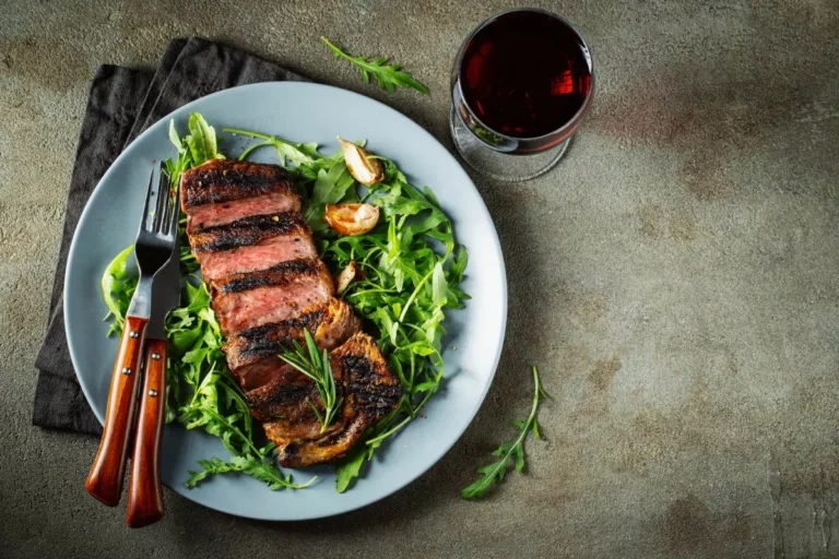 Grilled steak served on a bed of fresh arugula with a glass of red wine on the side.