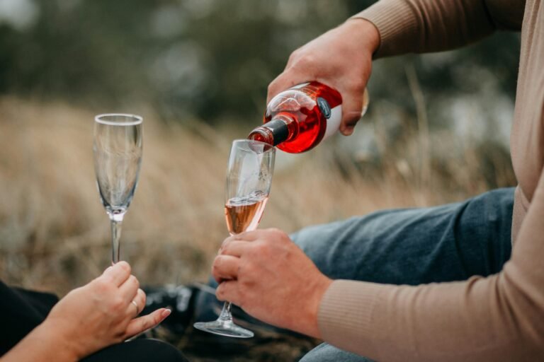 Close-up of a person pouring rosé wine into a glass during an outdoor picnic.