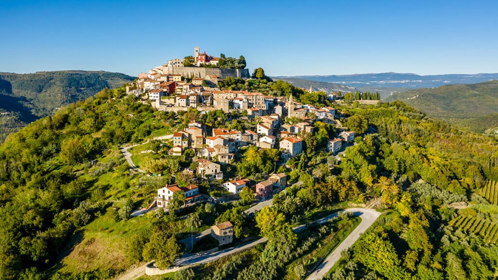 Aerial view of a picturesque hilltop town in Istria, surrounded by green countryside and rolling hills.