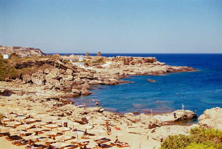 Beautiful rocky beach with sun loungers and umbrellas on a clear summer day, overlooking the turquoise sea.